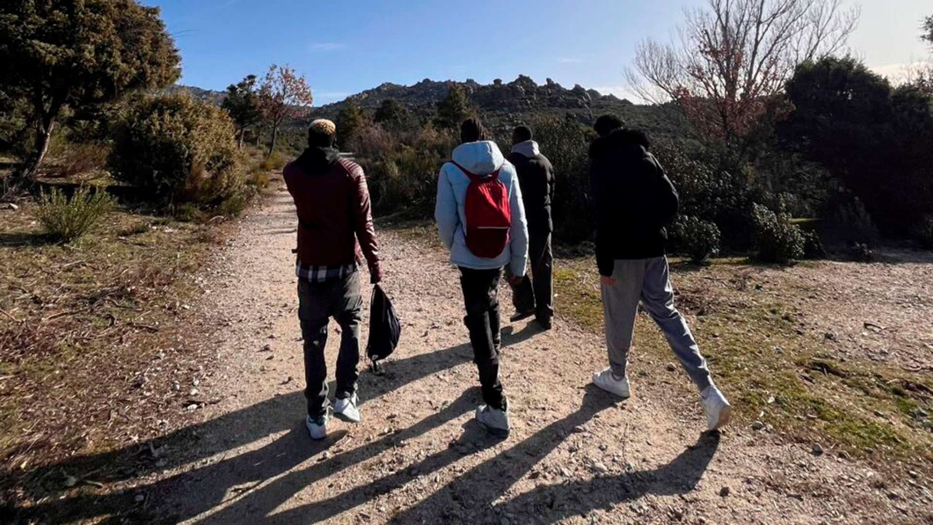 Cuatro jóvenes de espaldas caminando en la montaña.