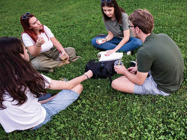 Un grupo de jóvenes charlando sentados en el césped de un parque.