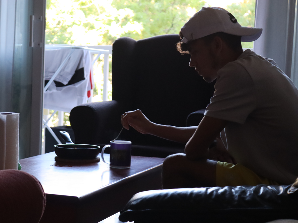 Un joven extutelado sentado en el sofá de su piso de emancipación de Camins Fundació removiendo una taza de café.