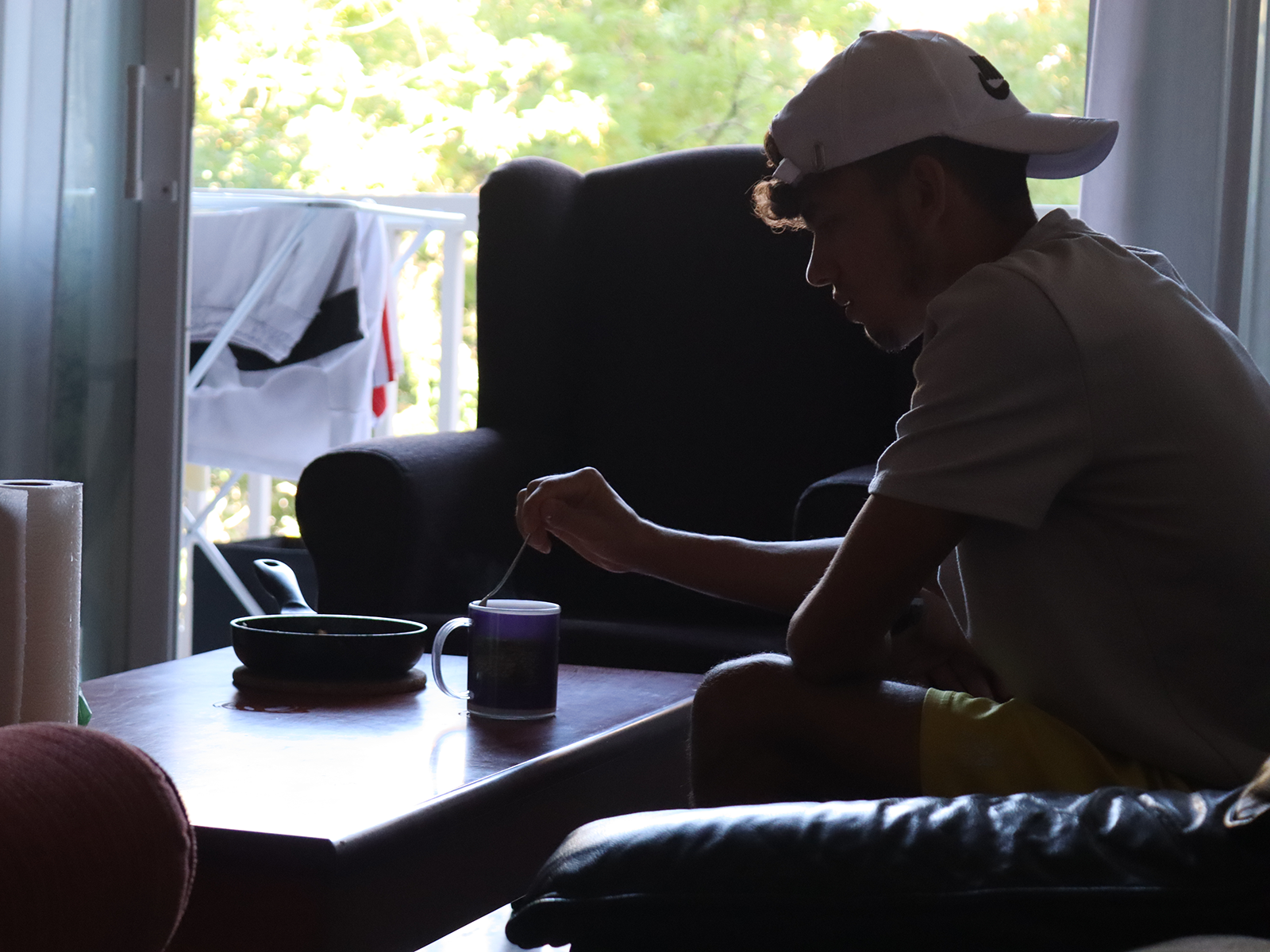 Un joven extutelado sentado en el sofá de su piso de emancipación de Camins Fundació removiendo una taza de café.