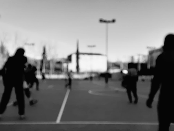 Foto muy pixelada y en blanco y negro en la que un grupo de jóvenes juega a fútbol en una pista de cemento .