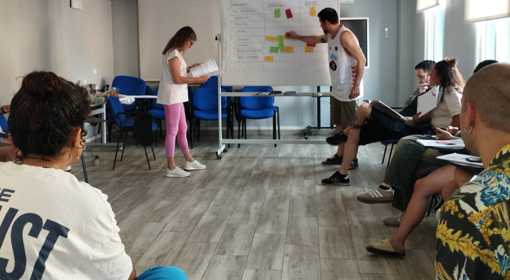 Dos profesionales exponen en la pizarra los resultados de la evaluación de indicadores durante los seminarios profesionales ante la mirada del resto de asistentes sentados en grupo.