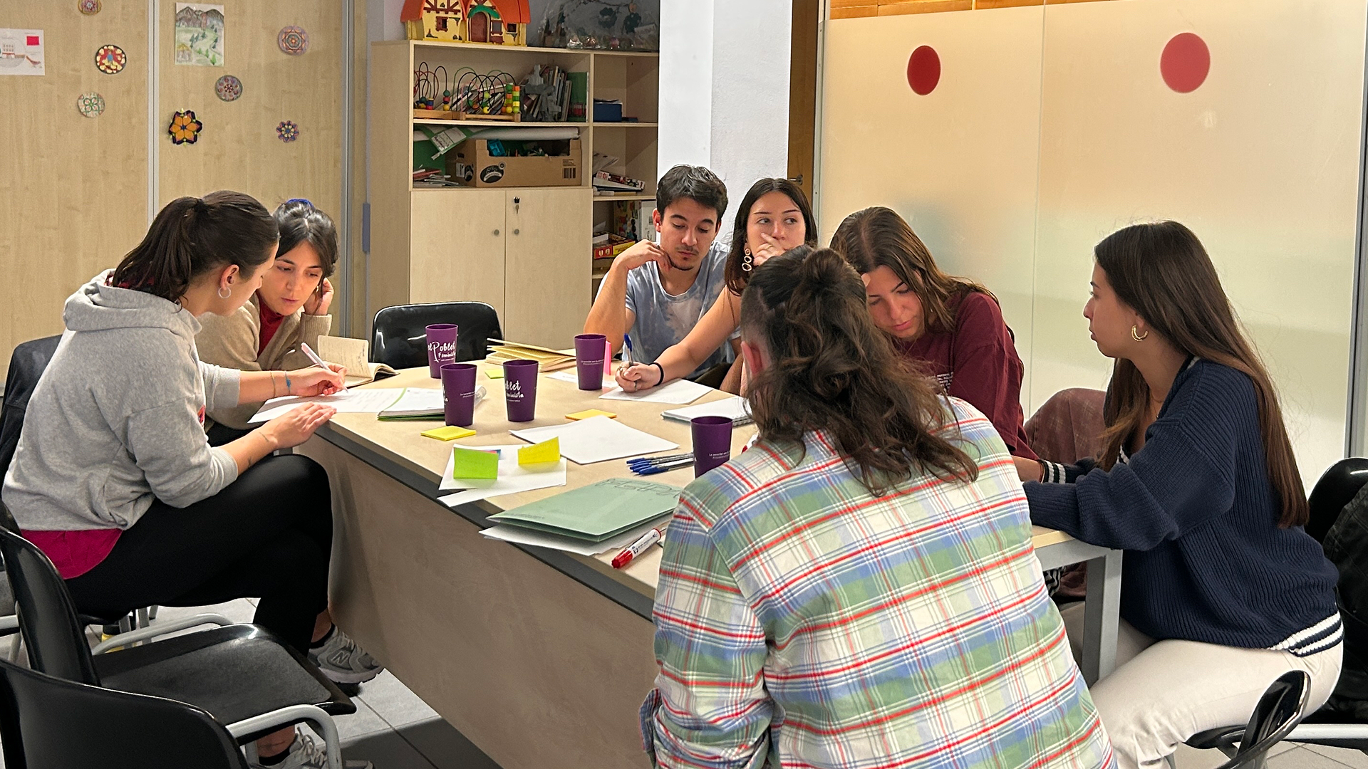 Siete personas jóvenes alrededor de una mesa realizando una dinámica de trabajo con post.its de colores.