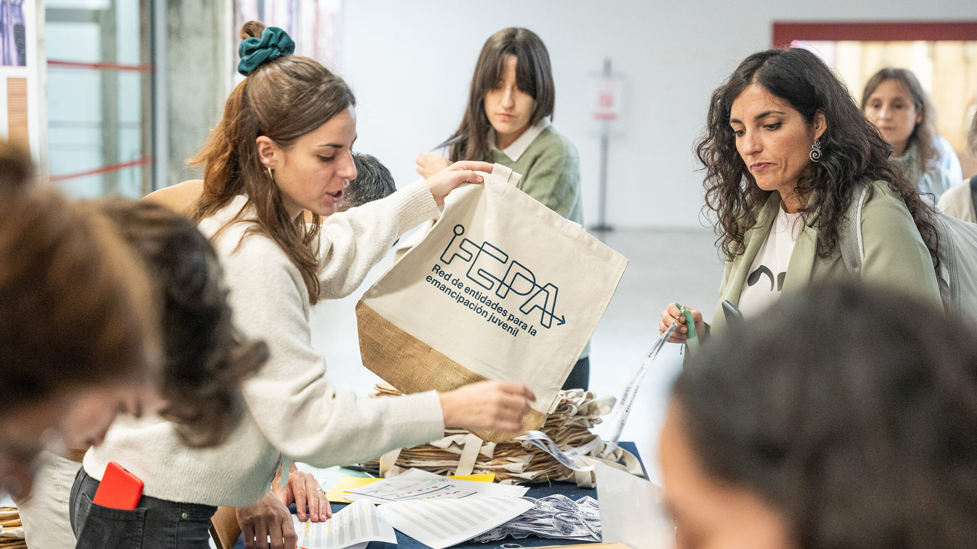 Una profesional del equipo de FEPA entrega una tote bag entrega una tote bag a una asistente a las XVIII jornadas FEPA en la mesa de acreditaciones.