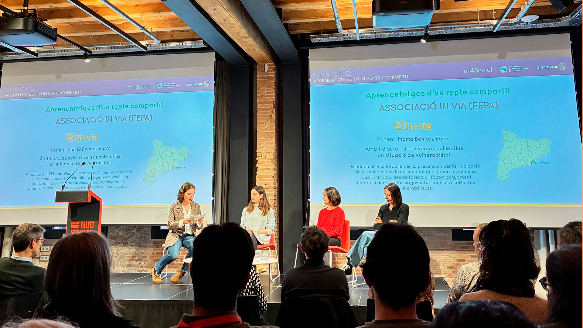 Escenario de las jornadas de SimbioTic organizadas por la Taula del Tercer Sector en el que se ve a cuatro ponentes, entre ellas, Marta Benítez de la Associació In Via.