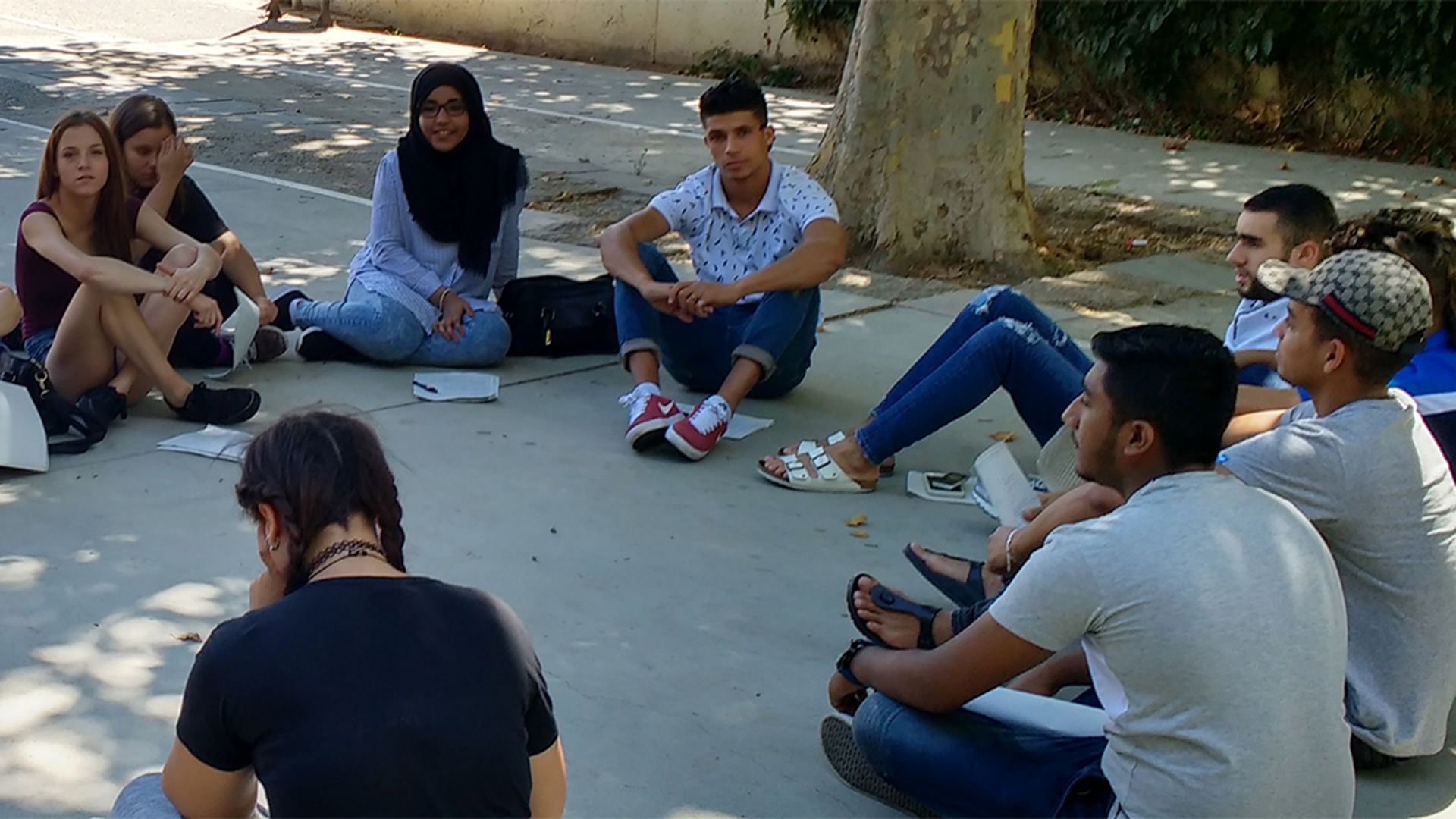 Un grupo de jóvenes extutelados sentados en el suelo en corro en una plaza.