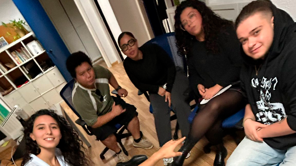 Cinco jóvenes reunidos en círculo y mirando a cámara.