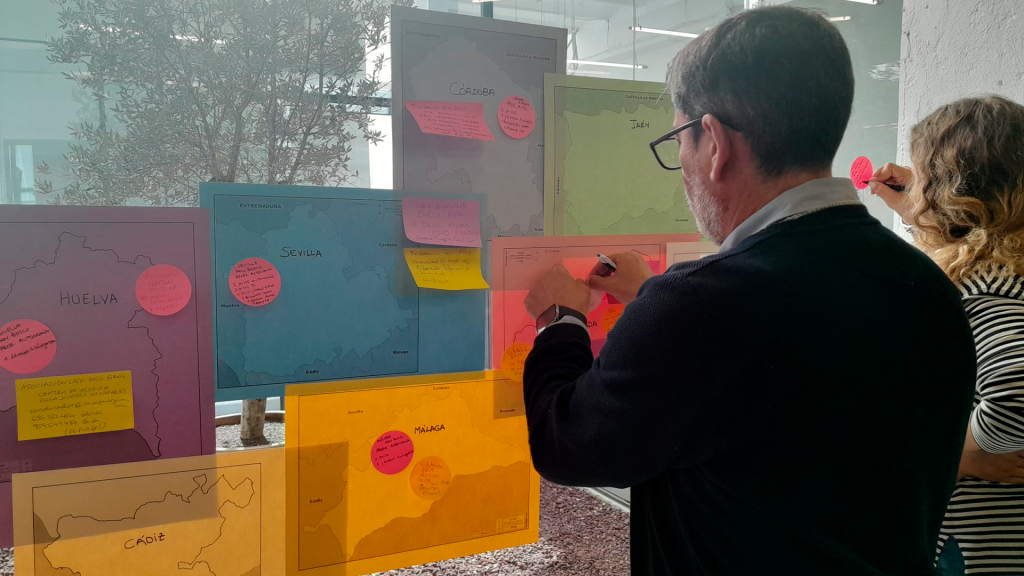 Dos representantes de entidades de la red FEPA en andalucía cuelgan post-its en una cristalera, en el marco de una dinámica para identificar los recursos disponibles para juventud extutelada en la comunidad.