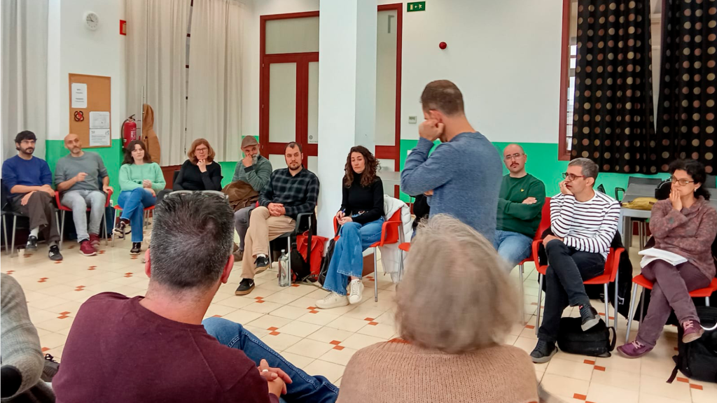 El formador, visto de lateral, pasea en el espacio que ha dejado el alumnado sentado en círculo.