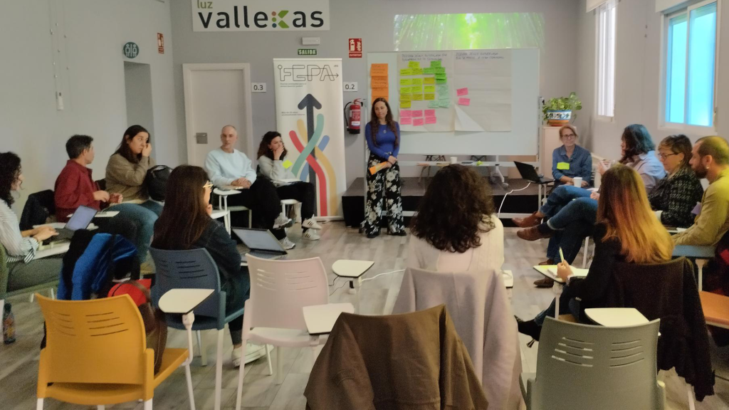 Profesionales de las entidades participantes sentados en círculo en un aula, atentos a la explicación de la dinamizadora.