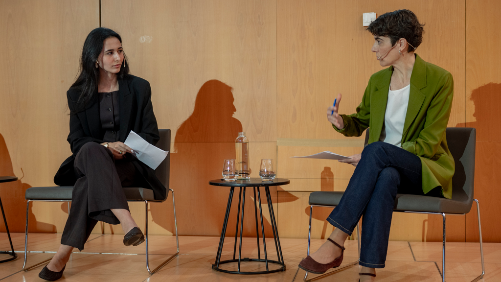 La dinamizadora de Entre Joves, Romaisa Krima y la Secretaria de Estado de Derechos Sociales, Rosa Martínez, sentadas en el escenario de las jornadas y conversando entre ellas.